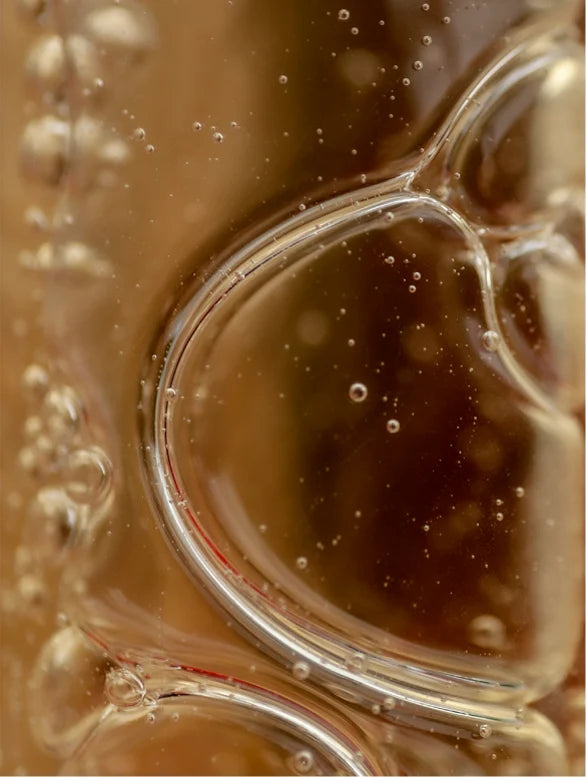 Close-up of a glass mug with a brown liquid and bubbles.