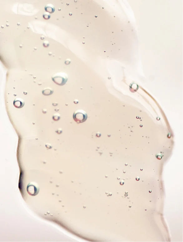 Close-up of a beige-colored skincare product with bubbles on a light pink background